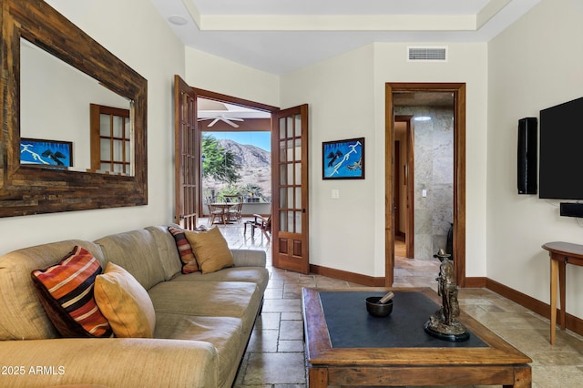 living area with stone tile flooring, baseboards, a ceiling fan, and visible vents