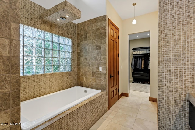 bathroom with a spacious closet, tile patterned floors, a bath, and tile walls