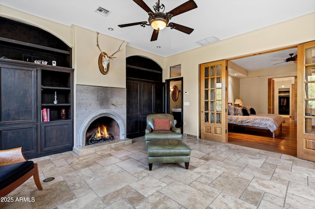 living area featuring visible vents, a ceiling fan, a tile fireplace, and stone tile flooring