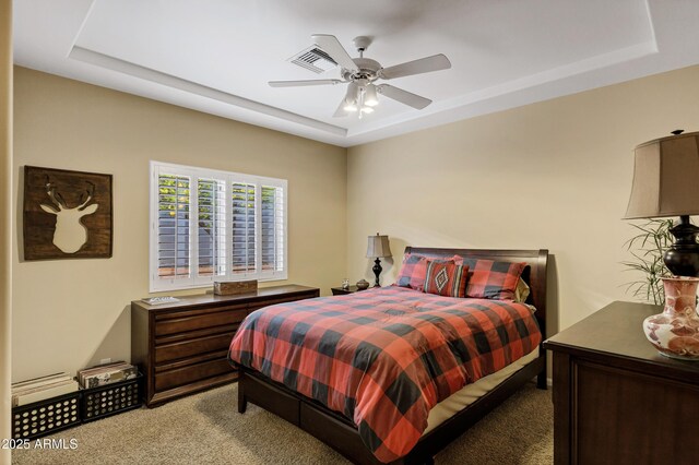 carpeted bedroom featuring a raised ceiling and a ceiling fan