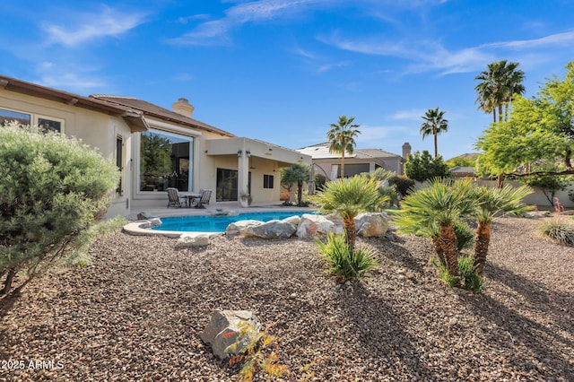 rear view of property featuring a chimney, fence, a patio, stucco siding, and an outdoor pool