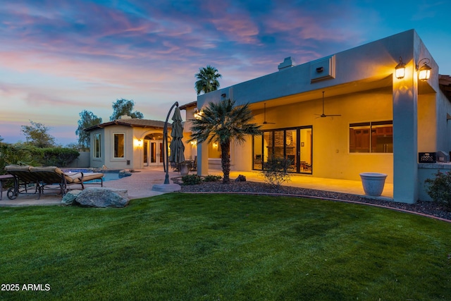 back of house at dusk with ceiling fan, a yard, a patio area, and stucco siding