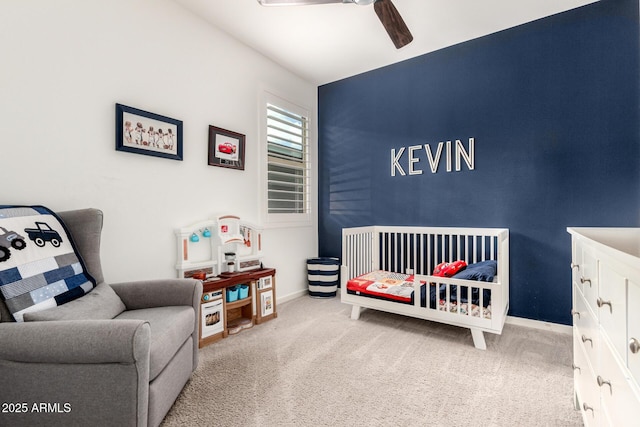 carpeted bedroom featuring baseboards, a crib, and a ceiling fan