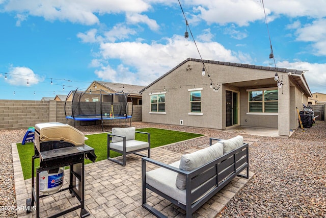 rear view of property featuring a patio, a trampoline, a fenced backyard, and an outdoor living space