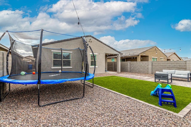 rear view of property with an outdoor living space, a trampoline, a lawn, and a patio area