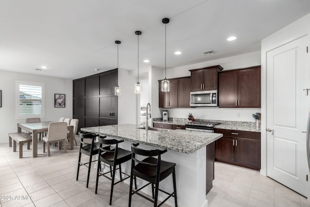 kitchen featuring visible vents, dark brown cabinetry, a breakfast bar area, appliances with stainless steel finishes, and a sink