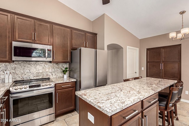 kitchen with light stone counters, a center island, lofted ceiling, appliances with stainless steel finishes, and a kitchen bar