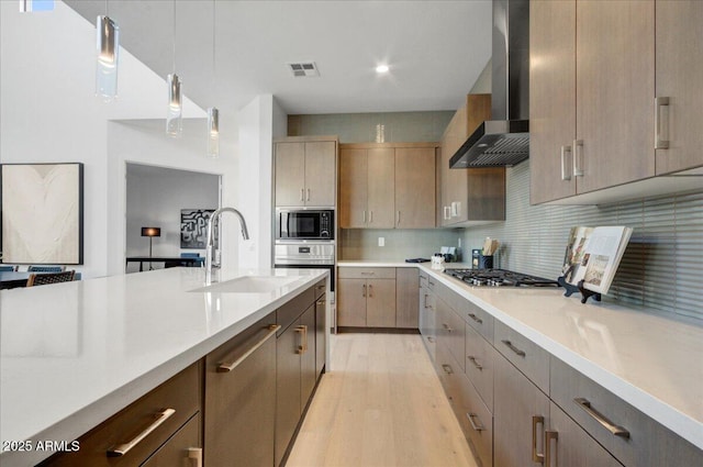 kitchen featuring pendant lighting, sink, stainless steel appliances, decorative backsplash, and wall chimney exhaust hood