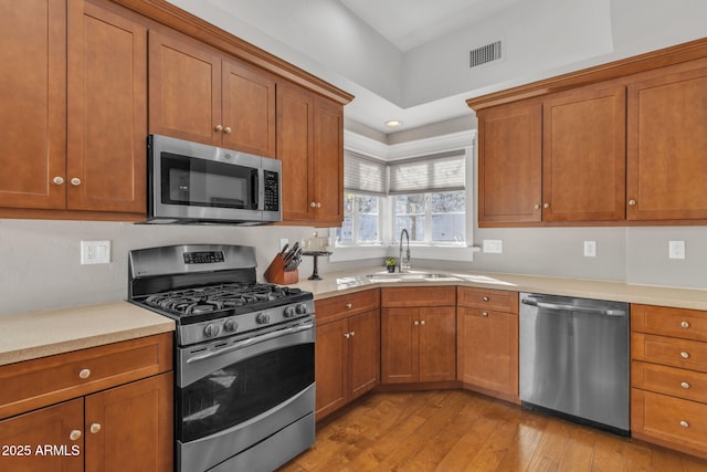 kitchen featuring appliances with stainless steel finishes, brown cabinets, visible vents, and a sink