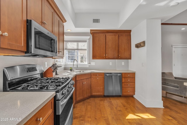 kitchen with a sink, visible vents, light wood-style floors, appliances with stainless steel finishes, and brown cabinetry