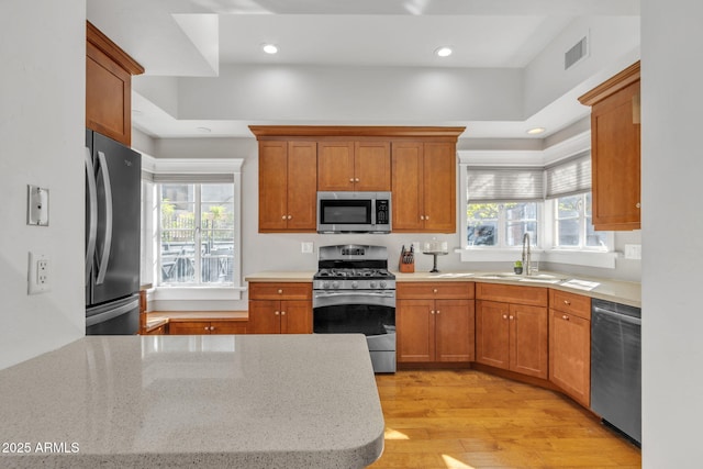 kitchen featuring stainless steel appliances, light wood-type flooring, a sink, and brown cabinets