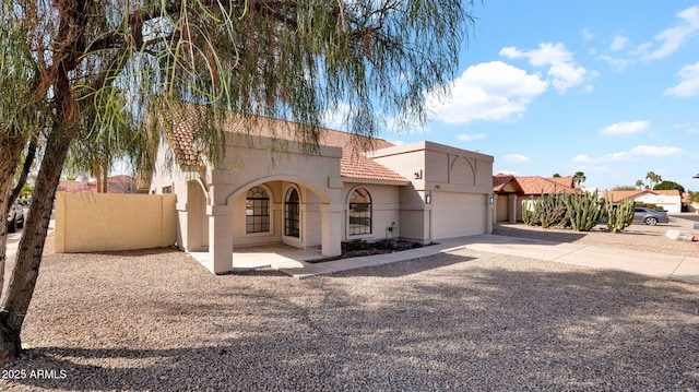 mediterranean / spanish-style home with a tile roof, driveway, fence, and stucco siding