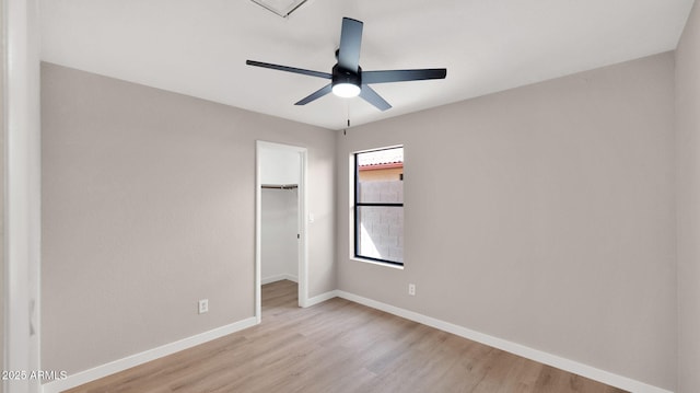 unfurnished bedroom with a closet, a spacious closet, a ceiling fan, light wood-type flooring, and baseboards