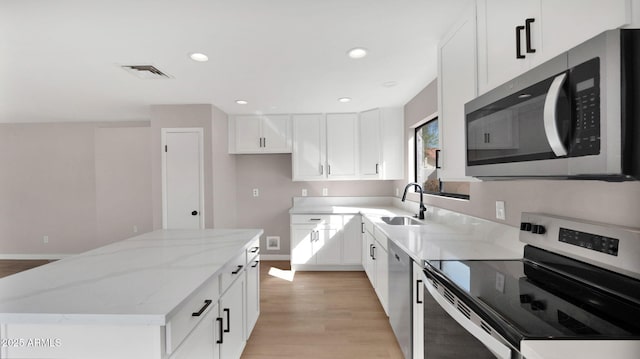 kitchen with light stone counters, stainless steel appliances, visible vents, a kitchen island, and a sink