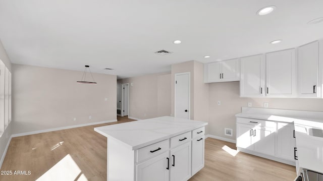 kitchen with recessed lighting, a kitchen island, white cabinets, light wood-type flooring, and light stone countertops