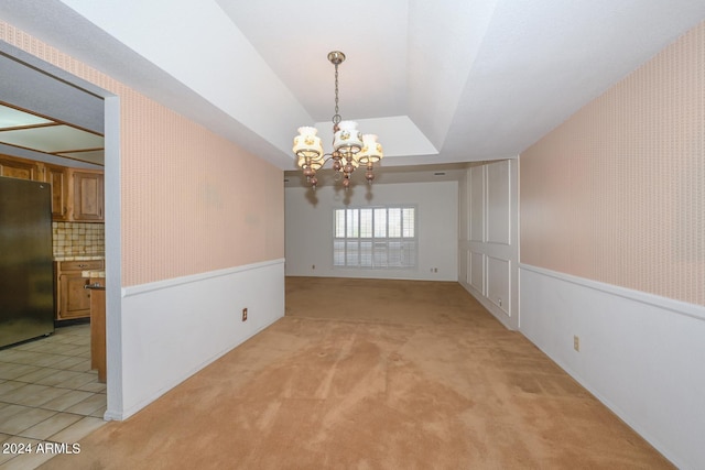 spare room featuring light carpet, a raised ceiling, vaulted ceiling, and a notable chandelier