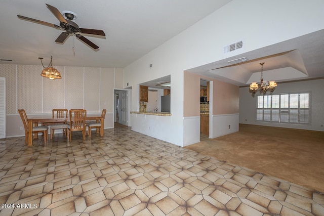 interior space with light colored carpet, a raised ceiling, and ceiling fan with notable chandelier