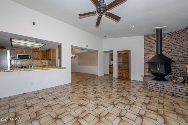 unfurnished living room with ceiling fan and a wood stove