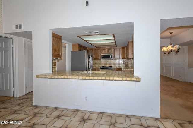 kitchen featuring appliances with stainless steel finishes, kitchen peninsula, an inviting chandelier, and decorative backsplash