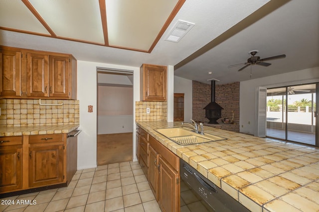 kitchen featuring a wood stove, tile counters, sink, ceiling fan, and decorative backsplash