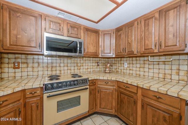 kitchen with light tile patterned floors, tile countertops, white electric range oven, and tasteful backsplash