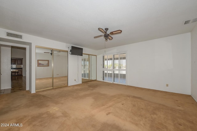 unfurnished bedroom with ceiling fan, light carpet, and multiple closets