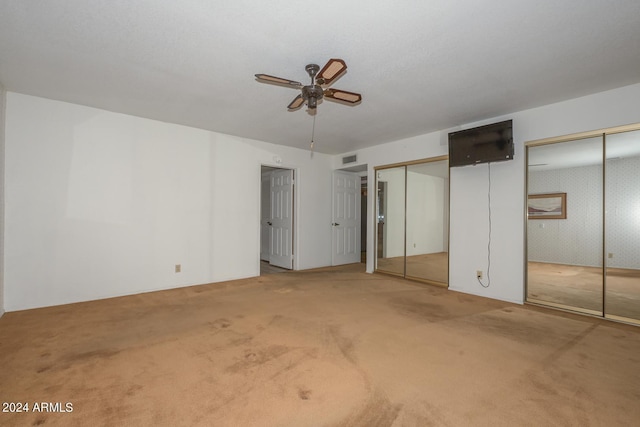 unfurnished bedroom with ceiling fan, light carpet, and multiple closets