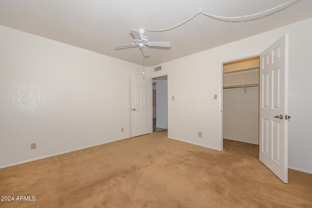 unfurnished bedroom featuring light colored carpet, ceiling fan, a walk in closet, and a closet