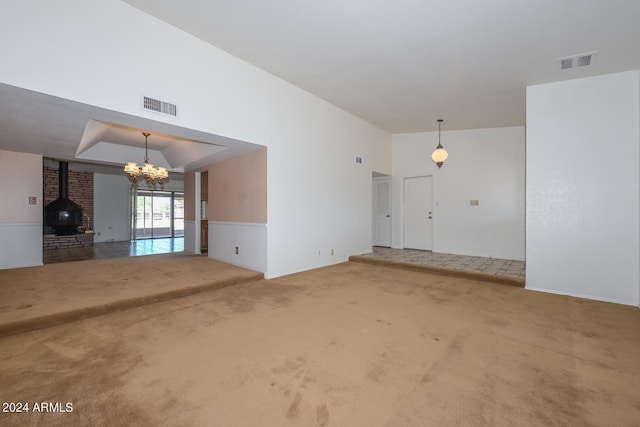 unfurnished living room featuring lofted ceiling, an inviting chandelier, a wood stove, and carpet