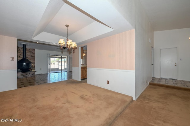 empty room with a wood stove, carpet, an inviting chandelier, and a tray ceiling