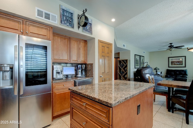 kitchen featuring brown cabinets, a center island, light tile patterned floors, stainless steel refrigerator with ice dispenser, and visible vents