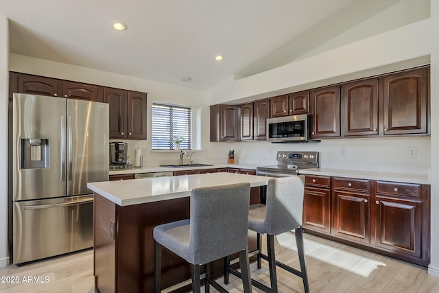 kitchen featuring stainless steel appliances, a sink, vaulted ceiling, light countertops, and a kitchen bar