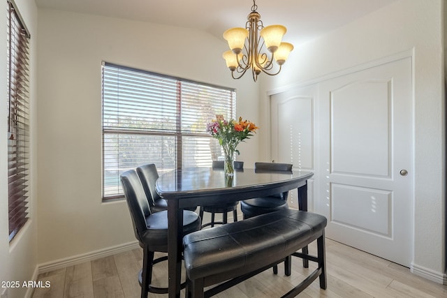 dining space featuring light wood-style flooring, baseboards, and a notable chandelier