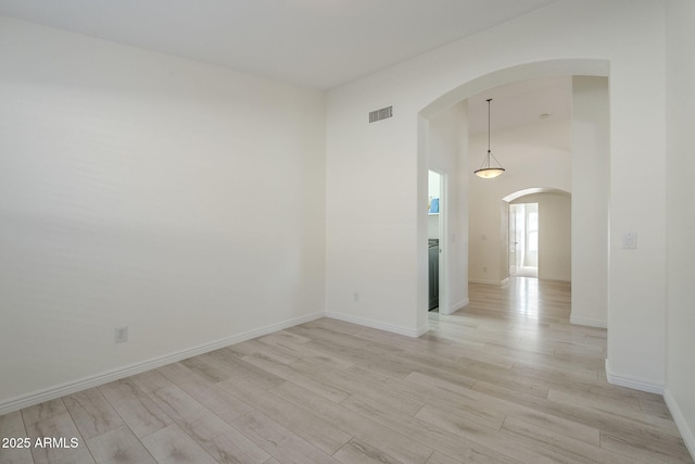 unfurnished room featuring arched walkways, baseboards, visible vents, and light wood finished floors