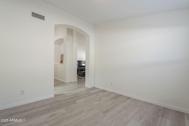 unfurnished room with light wood-style floors, baseboards, visible vents, and arched walkways