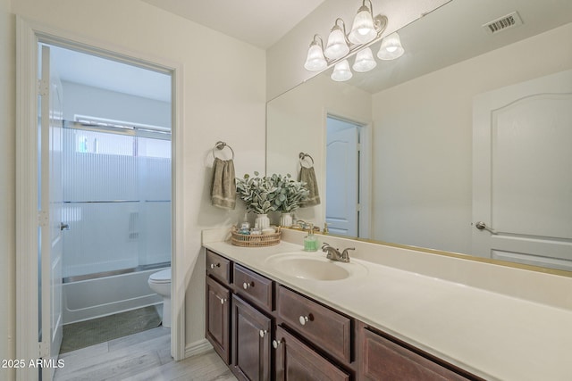 full bath with toilet, bath / shower combo with glass door, wood finished floors, vanity, and visible vents