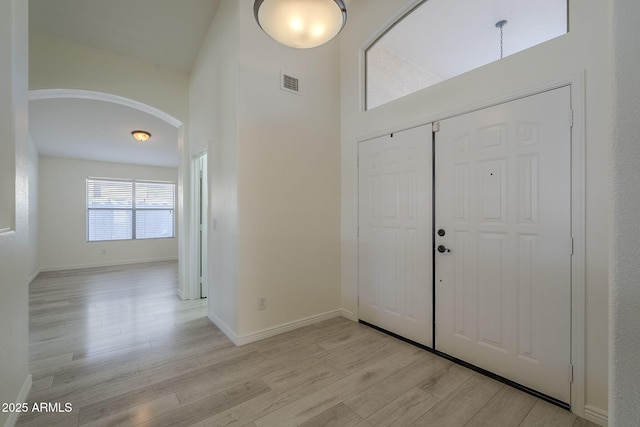 entrance foyer with arched walkways, baseboards, visible vents, and light wood finished floors