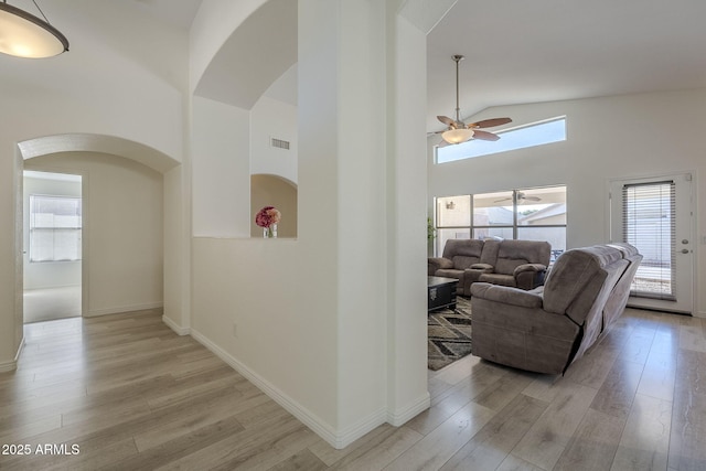 hall featuring visible vents, arched walkways, baseboards, light wood-type flooring, and high vaulted ceiling