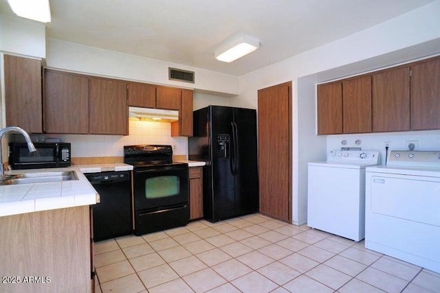 kitchen featuring a sink, separate washer and dryer, under cabinet range hood, visible vents, and black appliances