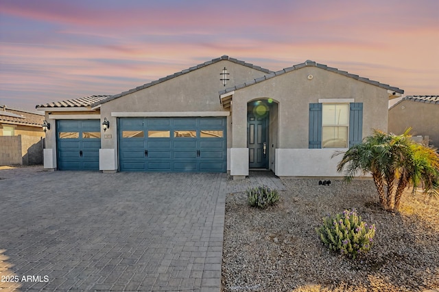 view of front of home with decorative driveway, a tile roof, an attached garage, and stucco siding