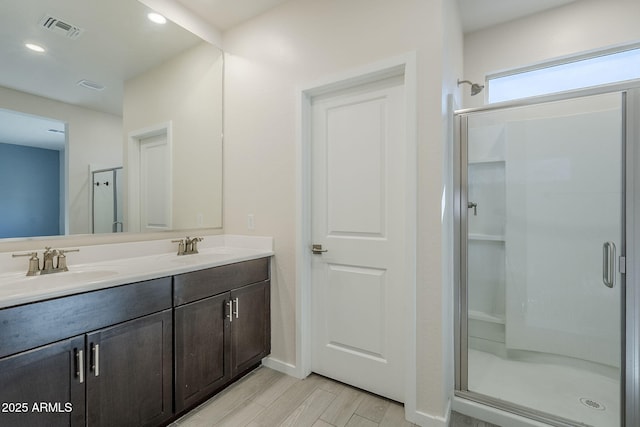 bathroom with visible vents, a sink, a shower stall, and wood finished floors