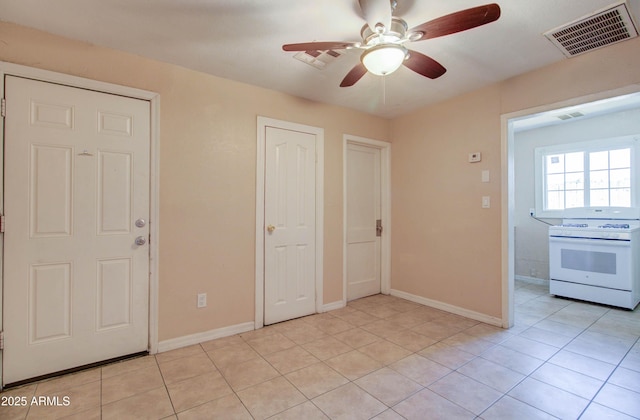 interior space featuring light tile patterned floors, ceiling fan, and white stove