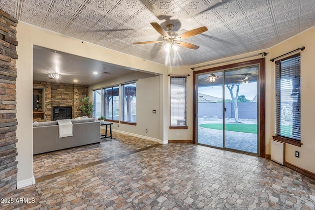 unfurnished living room featuring a stone fireplace and ceiling fan