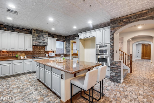 kitchen featuring white cabinetry, stainless steel appliances, a center island, a kitchen breakfast bar, and light stone counters