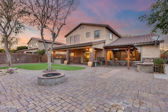 back house at dusk featuring area for grilling, a fire pit, and a patio