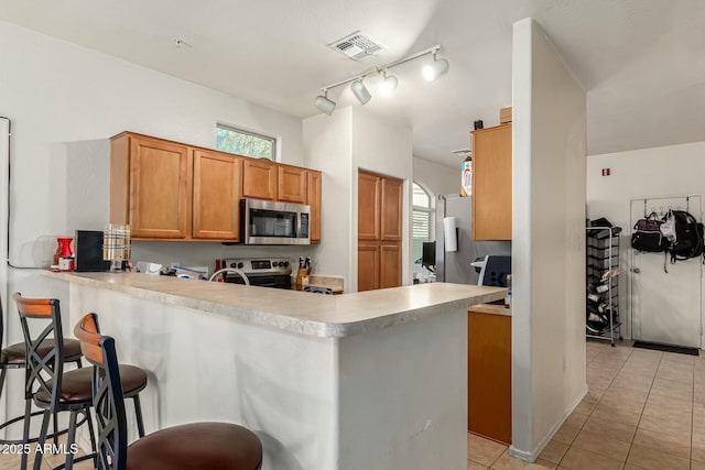 kitchen with light tile patterned floors, a kitchen breakfast bar, kitchen peninsula, and appliances with stainless steel finishes