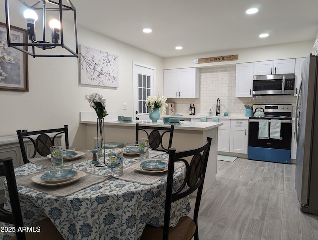 dining area with light wood-type flooring, sink, and a notable chandelier