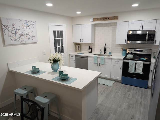kitchen with white cabinetry, kitchen peninsula, appliances with stainless steel finishes, a kitchen breakfast bar, and sink