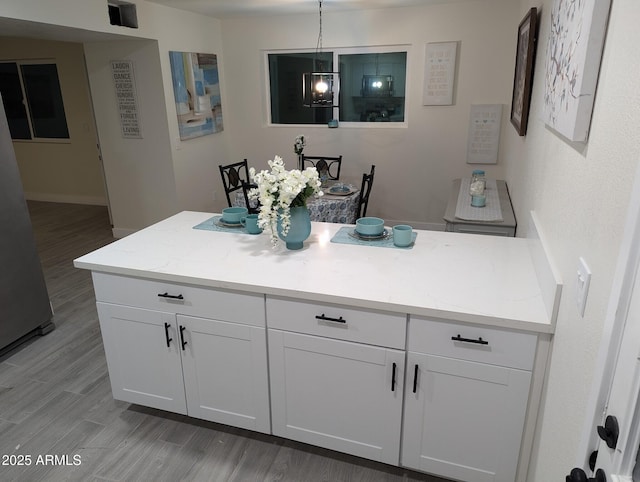 kitchen featuring light hardwood / wood-style floors, white cabinets, hanging light fixtures, and light stone countertops