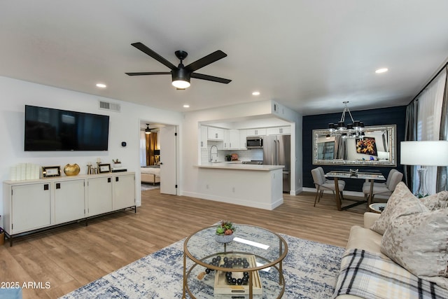 living area featuring ceiling fan with notable chandelier, recessed lighting, light wood-style floors, and visible vents